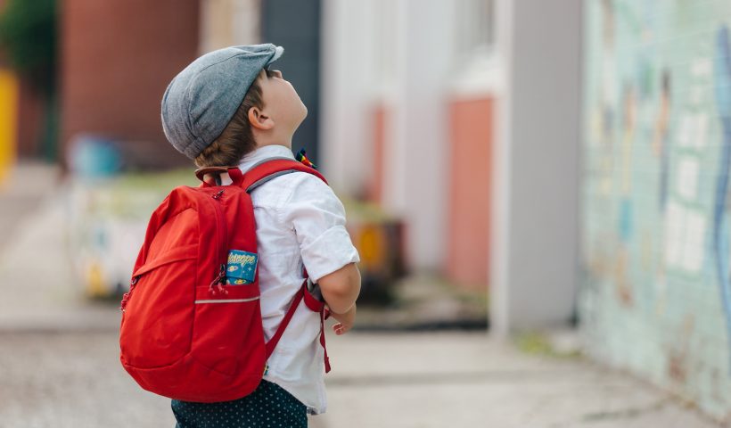 Little boy with a red backpack looking up. Photo by Matthew Henry